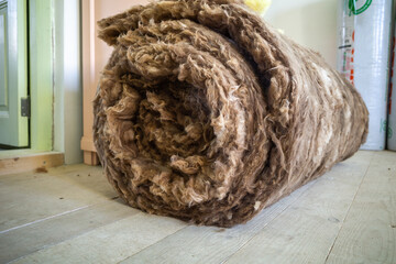 roll of mineral wool insulation on the wooden floor of a house under construction - obrazy, fototapety, plakaty