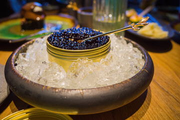 Black sturgeon caviar in a jar with ice in a metal jar on a wooden table in a restaurant - obrazy, fototapety, plakaty