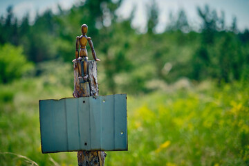 Wooden mannequin sits stump with tin plate stuffed on stump for text.