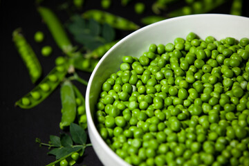 Shelled green peas in a large bowl against a dark background. Selective focus. Top view.