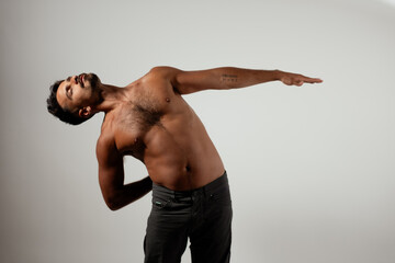 A man leans back, showing his muscular physique and reaching directly out with one hand, while...