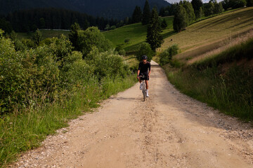 Obraz premium Professional cyclist practicing on gravel road.Male cyclist wearing black cycling kit and helmet.Man riding gravel bike on gravel road in mountains with scenic view.Gravel adventure.
