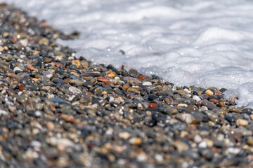 Colored pebbles on the beach of Greece with the waves of the sea covering them during a sunny day.