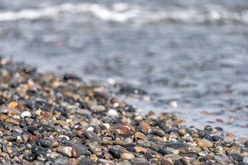 Colored pebbles on the beach of Greece with the waves of the sea covering them during a sunny day.