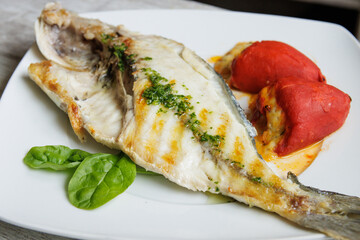 Grilled gilt-head bream on a white plate accompanied by stuffed piquillo peppers