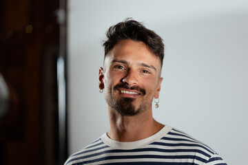 With a goatee and an earring, an adult man poses for a portrait in a studio space.