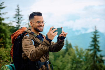 Happy backpacker takes pictures with smart phone while hiking in mountains.