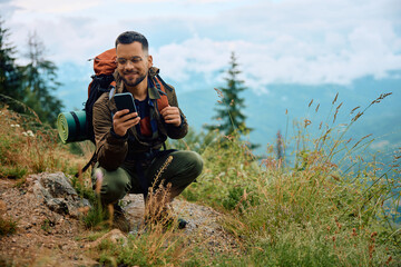 Happy hiker using cell phone while relaxing on hill.