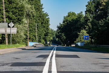 Asfaltowa droga idąca przez most nad rzeką Odrą otoczona barierkami wokół oświetlenie uliczne oraz nieliczne drzewa a na tle błękitne lekko zachmurzone niebo w zachodniej Polsce	 - obrazy, fototapety, plakaty