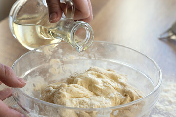 Close-up of female hands adding oil to dough on flour background, bread baking concept.