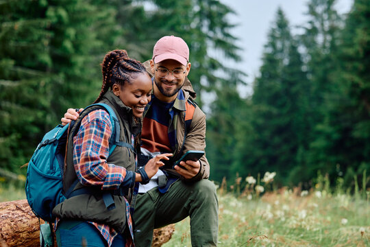 Young happy couple using cell phone while hiking in woods.