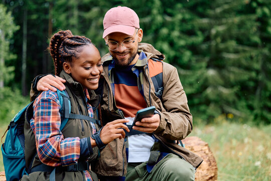 Happy multiracial couple of hikers using mobile phone in nature.