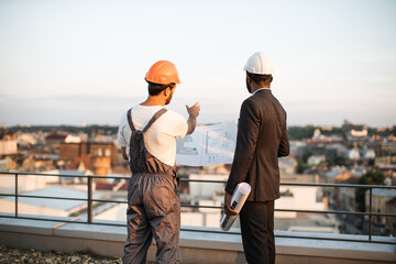 Rare view of caucasian bearded workman presenting design blueprints to african american urban...