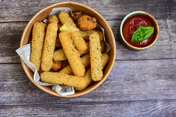 Vegetarian iitalian cheese breaded  oven baked  mozzarella sticks with  fresh basil on wooden background.Italian street food.