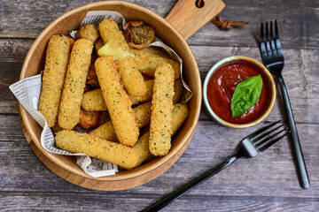Vegetarian iitalian cheese breaded  oven baked  mozzarella sticks with  fresh basil on wooden background.Italian street food.