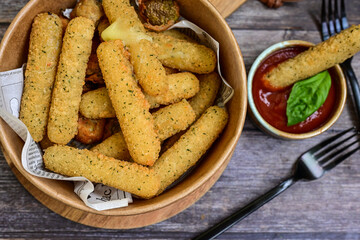 Vegetarian iitalian cheese breaded  oven baked  mozzarella sticks with  fresh basil on wooden background.Italian street food.