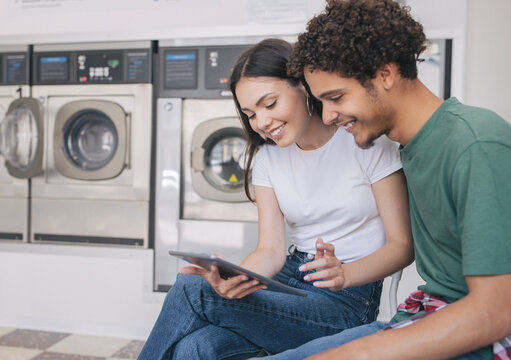 Happy Hispanic Couple Using Digital Tablet While Doing Laundry Indoor - Powered by Adobe