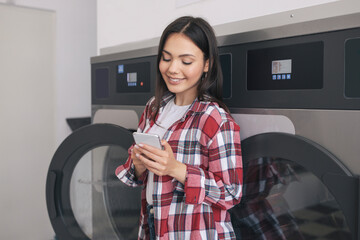 Happy Student Woman Doing Laundry And Texting On Cellphone Indoors