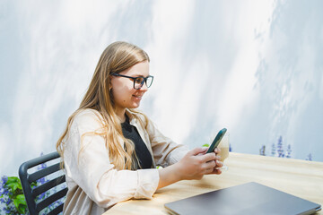 A woman manager sits on an outdoor terrace in a cafe and works online with coffee. Female...