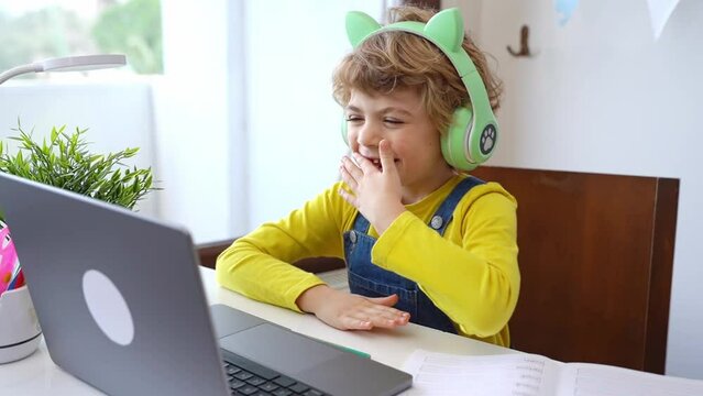 Cute smart caucasian primary School Child with headphones educate online laptop. Tutor teaching digital class, web lesson on computer at home. Virtual education course. Schoolboy girl studying doing