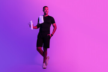 Black sportsman with bottle of water and towel, purple background