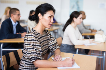Focused japanese woman listening carefully and taking notes during lecture at adult education class