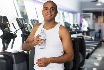 Fototapeta na wymiar Positive man resting after exercises in fitness gym drinking water