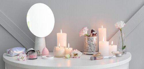 Burning aroma candles with mirror and makeup cosmetics on dressing table in room