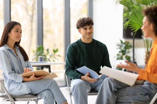 Happy international university students having a group discussion sitting together in circle of chairs and talking