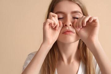 Young woman doing face building exercise on beige background, closeup