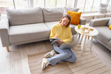 Female student studying with notebook and laptop at home