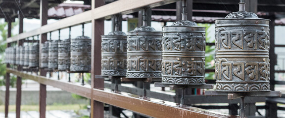 A row of prayer drums decorated with Buddhist symbols and writings on the territory of the datsan, a Buddhist temple. Religious prayer wheel for meditation in a Buddhist temple in Buryatia.Banner