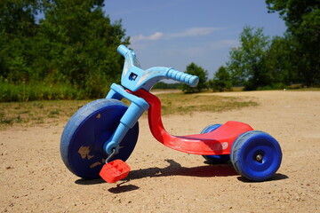 Blue and red used toddler tricycle big wheel bike sitting outside.