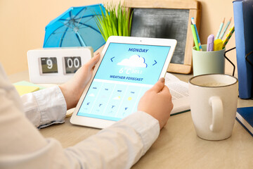 Woman with tablet computer checking weather forecast at table, closeup