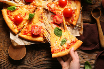 Woman taking slice of tasty pizza margarita on wooden table