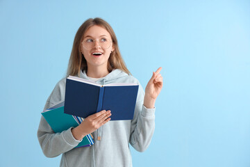 Obraz premium Happy female student with different books pointing at something on blue background