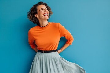 cheerful young woman in orange sweater and skirt on blue background