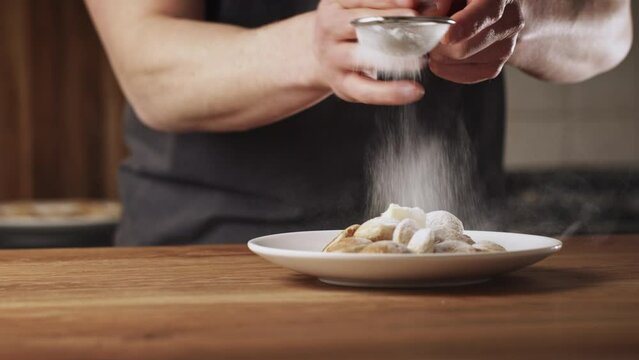 A man serving freshly made poffertjes with powdered sugar at home. Traditional Dutch mini pancakes with buckwheat flour, white flour, egg and milk.