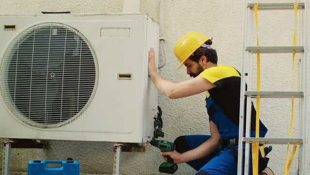 Experienced wireman dissasembling external air conditioner metal side coil panel to check for bad wiring. Meticulous electrician doing repairing on malfunctioning hvac system