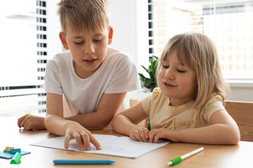 The older brother teaches the younger sister to read letters. Brother and sister, home schooling.