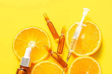 Ampoules with vitamin C, syringe, bottle of essential oil and orange slices on yellow background,...