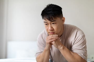 Closeup of depressed chinese middle aged man sitting on bed