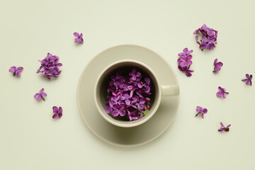 Obraz na płótnie Canvas Cup with beautiful lilac flowers on beige background