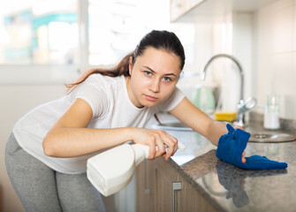 Portrait of young positive woman doing chores cleaning kitchen