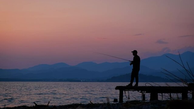 Working fisherman silhouette on pier. A man silhouette stay on the beach and catch the fish during sunset. A concept of fishing men hobby.