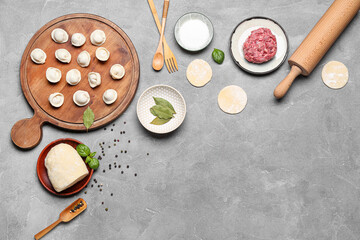 Wooden board with uncooked dumplings and ingredients on grey background
