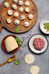 Wooden board with uncooked dumplings and ingredients on grey background