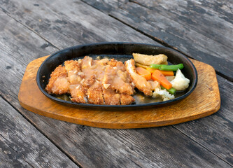 Sliced fried chicken at the hot plate, with vegetables, on an old vintage wooden table