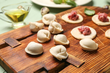 Wooden board with uncooked dumplings on table