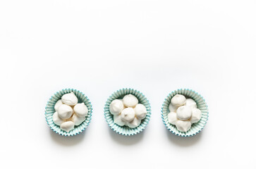White mini meringue cookies in blue paper cup on white background.